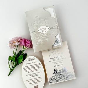 May include: Elegant wedding invitation suite featuring a light gray embossed floral design. Includes an invitation, details card, and RSVP card. The invitation is tied with a string and features the names "Hannah" and "Jack".