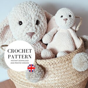 May include: A crochet pattern for a bunny, with the text "CROCHET PATTERN" in a white circle. The image shows two plush bunnies in a woven basket with pom-poms. The bunnies are cream-colored with dark eyes and embroidered features.