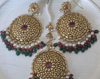 Puede incluir: Pendientes, collar y maang tikka dorados con piedras rosas y verdes y detalles de perlas.