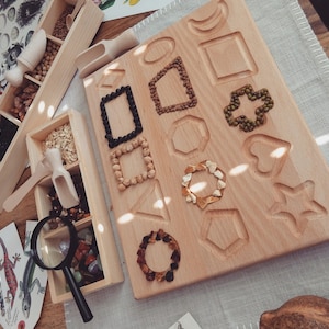 May include: A wooden board with various shapes cut out, filled with different types of beans and seeds. The board is made of light wood and has a natural finish. There are also several small wooden boxes filled with different types of beans and seeds.