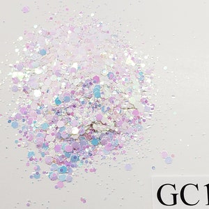 May include: A close-up of iridescent glitter in shades of white, pink, and blue. The glitter is scattered on a white background. The text "GC13" is visible in the lower right corner of the image.