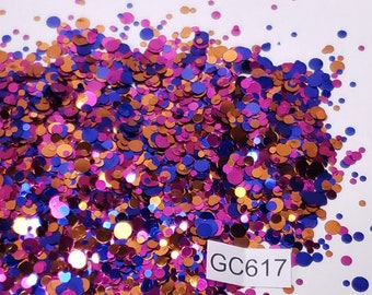 May include: A pile of colorful glitter in shades of pink, blue, and gold. The glitter is in the shape of small circles and is scattered on a white surface. The text "GC617" is visible on a white label.