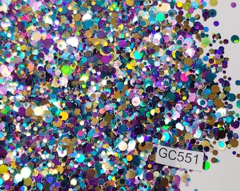 May include: A close-up of a pile of iridescent glitter in various shades of blue, green, gold, and purple. The glitter is in the shape of small circles and is arranged in a random pattern. The glitter is labeled "GC551".