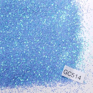 May include: Close-up of a pile of light blue glitter with iridescent sparkles. A small white label with the text "GC514" is in the lower right corner. The glitter is scattered across a white surface.