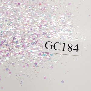 May include: White iridescent glitter with a variety of sizes and shapes. The glitter is scattered on a white background. A white label with the text "GC184" is in the lower right corner of the image.