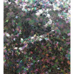 Puede incluir: Una imagen de primer plano de purpurina hologr&aacute;fica iridiscente en forma de estrella. La purpurina es una mezcla de verde, azul, morado y rosa.