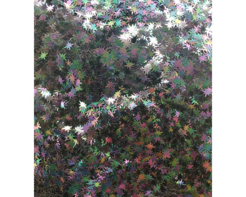 Puede incluir: Una imagen de primer plano de purpurina hologr&aacute;fica iridiscente en forma de estrella. La purpurina es una mezcla de verde, azul, morado y rosa.