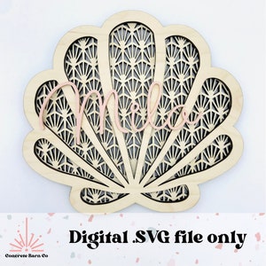 Könnte beinhalten: Eine Holzmuschel mit einem ausgeschnittenen geometrischen Muster, der Name "Mila" ist in rosa ausgeschnitten und auf die Muschel gelegt.