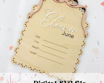 May include: A wooden baby announcement plaque with a pink bow and the name "Eleanor June" written in white cursive. The plaque has spaces to fill in the date, time, weight, and height of the baby.