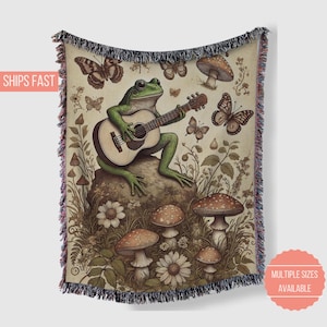 May include: A green frog playing a guitar in a whimsical forest setting. The frog is sitting on a rock surrounded by mushrooms, flowers, and butterflies. The guitar is brown with a light brown pickguard. The background is a light brown with a green and brown pattern.