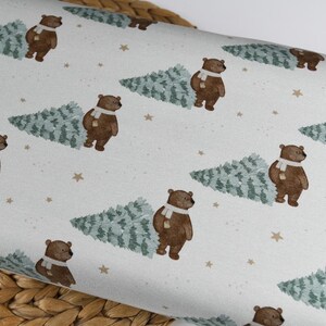 May include: A repeating pattern on a white background features brown bears wearing white scarves, each next to a green Christmas tree. Small tan stars are scattered across the surface, creating a festive, wintery design.