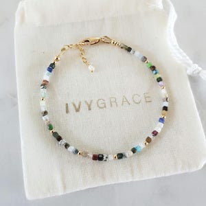 Puede incluir: Una pulsera delicada con pequeñas cuentas cuadradas multicolores intercaladas con diminutas esferas metálicas doradas. La pulsera incluye un cierre de mosquetón dorado y una cadena ajustable, sobre una bolsa de tela color crema con IVYGRACE impreso en dorado.