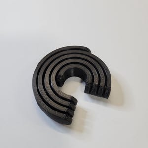 May include: A set of five black plastic rings stacked on top of each other, forming a rainbow shape.