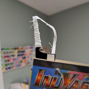 May include: A bookmark with a white fabric loop and a black and white rectangular base. The bookmark is inserted into a book with the title "InuYasha" in gold and red lettering on a blue background.