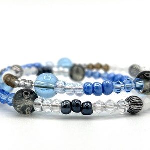 May include: A multi-strand bracelet with blue, clear, and silver beads. The bracelet features a variety of bead shapes and sizes, including round, square, and oval beads.