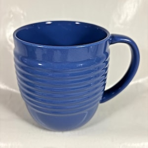 Peut inclure: Une tasse en céramique bleue avec un extérieur nervuré et une anse incurvée. La tasse a une finition brillante et une large ouverture. La tasse est conçue pour les boissons chaudes ou froides.