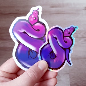 May include: Two iridescent purple and pink snake stickers. The snakes are curled up in a circle and have a holographic finish.