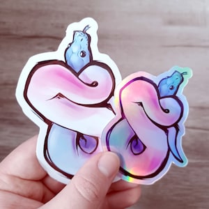 May include: Two iridescent stickers featuring a blue snake curled around itself. The sticker on the left is white with a pink hue, while the sticker on the right is pink with a blue hue.