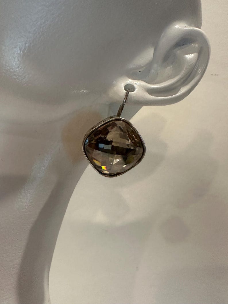 Peut inclure: Boucle d'oreille unique avec une pierre pr&eacute;cieuse en quartz fum&eacute;, carr&eacute;e et facett&eacute;e. La pierre est sertie dans un cadre en m&eacute;tal argent&eacute; et suspendue &agrave; un crochet simple. La boucle d'oreille est pr&eacute;sent&eacute;e sur fond blanc.