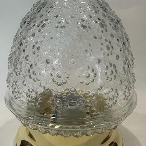 May include: A clear glass light fixture with a textured, bubble-like pattern on the shade. The base is a shiny gold color. The fixture has a classic, vintage design.