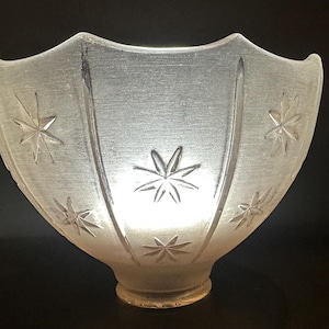 May include: A frosted glass light shade featuring a scalloped top edge and a series of etched starburst patterns. The bowl-shaped fixture has a narrow circular base and vertical ridges that separate the star motifs across the translucent surface.