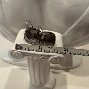 Peut inclure: Une paire de boucles d'oreilles carr&eacute;es en cristal gris fum&eacute; avec des crochets argent&eacute;s. Chaque boucle d'oreille mesure environ 2,5 cm de large. Les boucles d'oreilles sont pr&eacute;sent&eacute;es sur un pr&eacute;sentoir blanc.