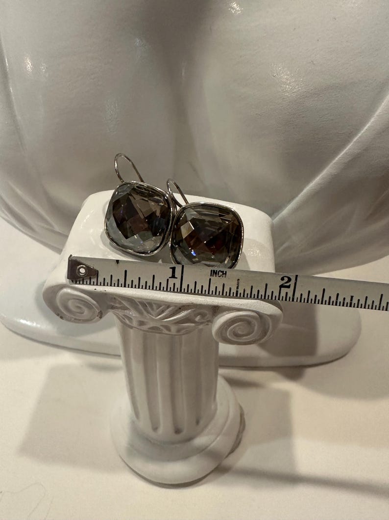 Peut inclure: Une paire de boucles d'oreilles carr&eacute;es en cristal gris fum&eacute; avec des crochets argent&eacute;s. Chaque boucle d'oreille mesure environ 2,5 cm de large. Les boucles d'oreilles sont pr&eacute;sent&eacute;es sur un pr&eacute;sentoir blanc.