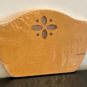 May include: A light brown wooden decorative piece, possibly a headboard or wall decor, with a curved top and a cut-out floral design. The wood grain is visible, and the item is wrapped in clear plastic.