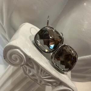 Peut inclure: Une paire de boucles d'oreilles carr&eacute;es en quartz fum&eacute; facett&eacute; avec des montures en m&eacute;tal argent&eacute;. Les boucles d'oreilles sont pr&eacute;sent&eacute;es sur un &eacute;l&eacute;ment architectural blanc de style classique.