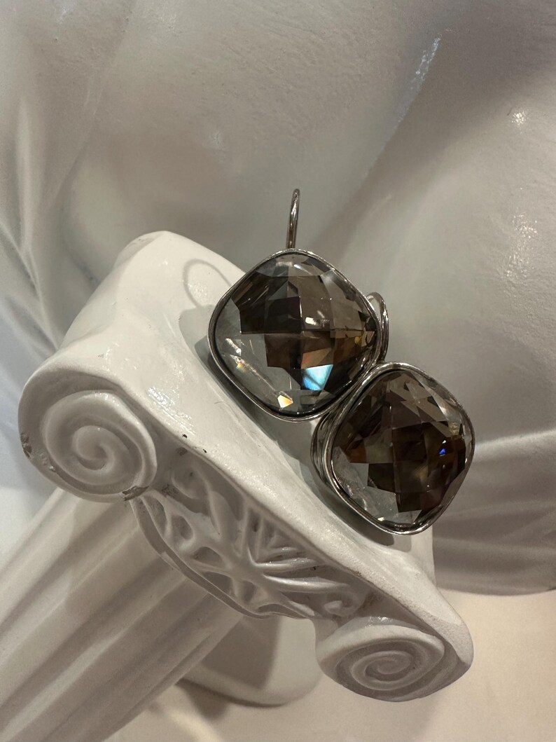 Peut inclure: Une paire de boucles d'oreilles carr&eacute;es en quartz fum&eacute; facett&eacute; avec des montures en m&eacute;tal argent&eacute;. Les boucles d'oreilles sont pr&eacute;sent&eacute;es sur un &eacute;l&eacute;ment architectural blanc de style classique.