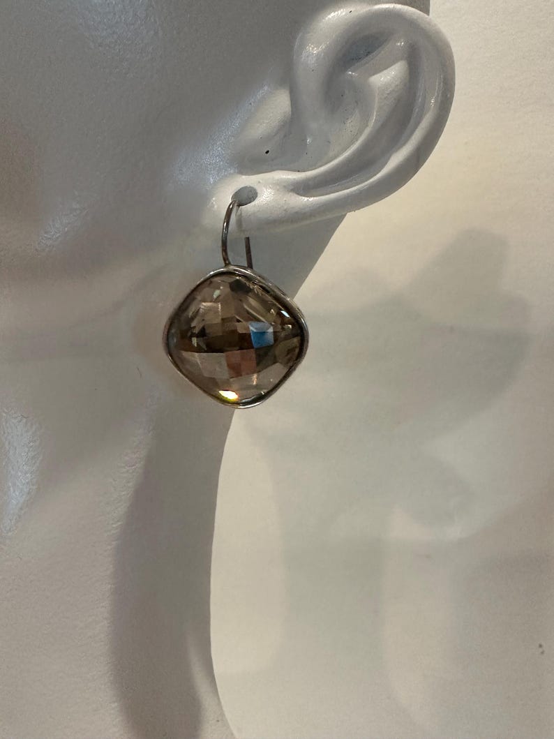 Peut inclure: Une boucle d'oreille unique avec une pierre pr&eacute;cieuse en quartz fum&eacute; taill&eacute;e en forme carr&eacute;e. La pierre est sertie dans un cadre en m&eacute;tal argent&eacute; et suspendue &agrave; un simple crochet. La boucle d'oreille est pr&eacute;sent&eacute;e sur fond blanc.