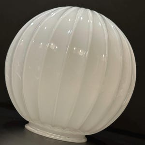 May include: A white, globe-shaped light fixture with vertical, ribbed detailing. The glass shade has a glossy finish and a rounded base. The fixture is designed to diffuse light and is suitable for various interior design styles.