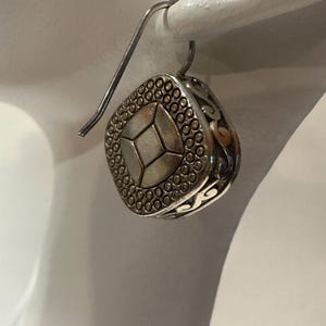 Peut inclure: Boucle d'oreille carr&eacute;e argent&eacute;e avec un motif g&eacute;om&eacute;trique. La boucle d'oreille pr&eacute;sente une forme de losange central entour&eacute;e de petits points. Les bords ont un motif ajour&eacute;. Elle est suspendue &agrave; un crochet d'oreille incurv&eacute;.