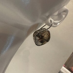 Peut inclure: Boucle d'oreille argent&eacute;e avec une pierre de quartz fum&eacute; carr&eacute;e et facett&eacute;e. La boucle d'oreille est fix&eacute;e &agrave; un crochet argent&eacute; et pr&eacute;sente un motif orn&eacute; de filigrane autour de la pierre pr&eacute;cieuse. La boucle d'oreille est pr&eacute;sent&eacute;e sur une t&ecirc;te de mannequin blanche.