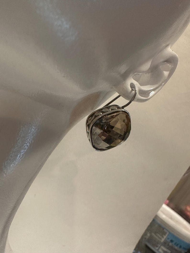 Peut inclure: Boucle d'oreille argent&eacute;e avec une pierre de quartz fum&eacute; carr&eacute;e et facett&eacute;e. La boucle d'oreille est fix&eacute;e &agrave; un crochet argent&eacute; et pr&eacute;sente un motif orn&eacute; de filigrane autour de la pierre pr&eacute;cieuse. La boucle d'oreille est pr&eacute;sent&eacute;e sur une t&ecirc;te de mannequin blanche.