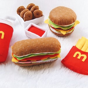 May include: Felt food set with a red cup, two hamburgers, french fries, and a box of chicken nuggets. The food is all made of felt and has a realistic appearance.