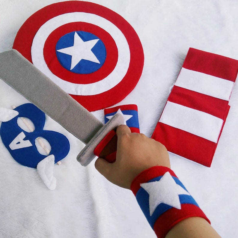 May include: A Captain America costume set for kids, featuring a red, white, and blue shield, a blue mask with a white star, a gray sword, a red and white striped scarf, and a red, white, and blue armband.
