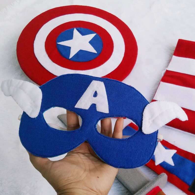 May include: A blue felt mask with a white 'A' and white wings, a red and white felt shield with a white star, and a red and white felt armband with a white star.