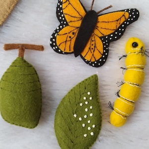 May include: Felt craft set featuring a yellow caterpillar, a green cocoon, a green leaf with white dots, and a black and orange butterfly.