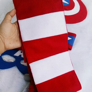 May include: Red and white striped fabric armband with three white stripes. The armband is made of felt and is a popular accessory for superhero costumes.