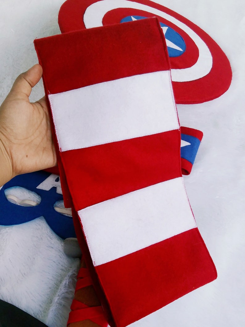 May include: Red and white striped fabric armband with three white stripes. The armband is made of felt and is a popular accessory for superhero costumes.