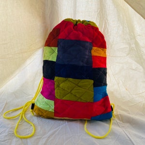 May include: A colourful patchwork drawstring bag with a yellow cord. The bag is made of different coloured fabrics, including red, green, blue, and purple.