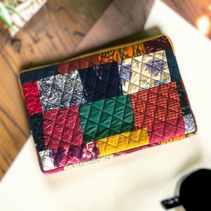 May include: A rectangular quilted pouch featuring a patchwork design of various fabric squares in colors including deep red, forest green, mustard yellow, navy blue, and black, with intricate floral and geometric patterns throughout the textile.