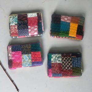 May include: Four quilted patchwork zipper pouches in shades of pink, red, green, blue, and yellow. Each pouch features a unique arrangement of fabric squares with various patterns and textures. The pouches are rectangular and have a quilted design.