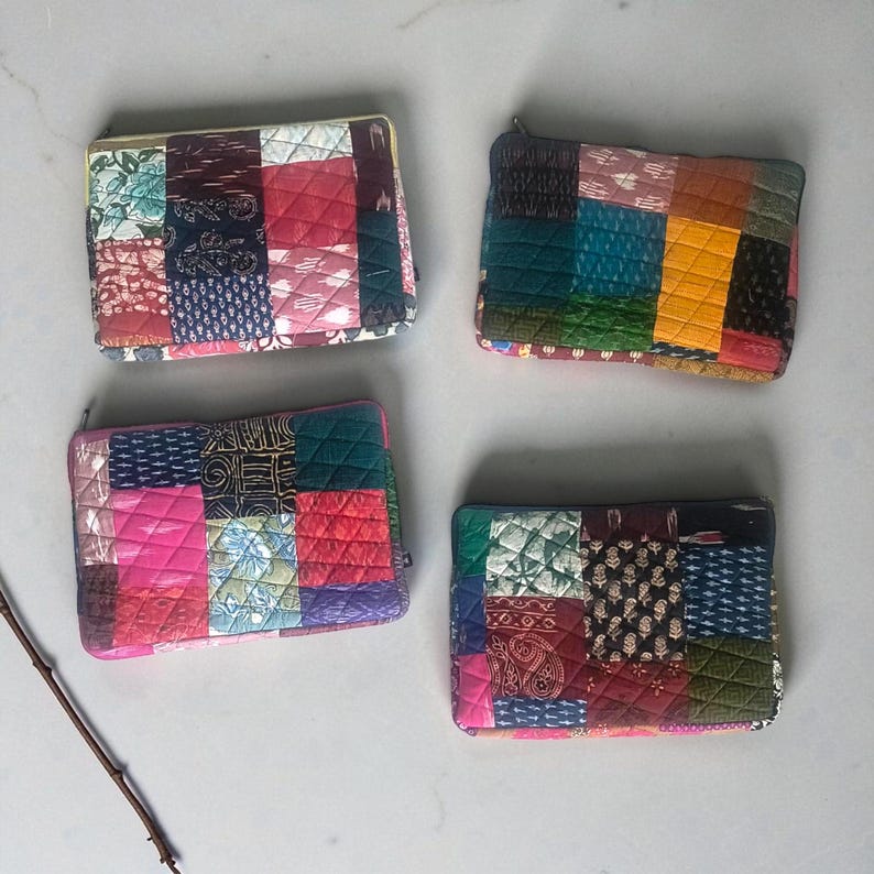 May include: Four quilted patchwork zipper pouches in shades of pink, red, green, blue, and yellow. Each pouch features a unique arrangement of fabric squares with various patterns and textures. The pouches are rectangular and have a quilted design.