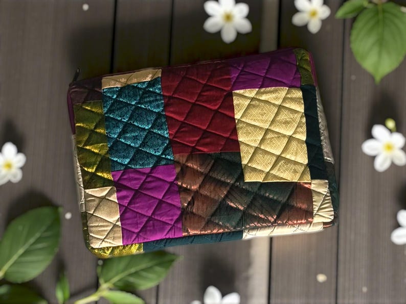 May include: A quilted clutch with a patchwork design. The clutch features a variety of colors, including gold, teal, purple, and red. The fabric has a diamond pattern. The clutch is rectangular and has a zipper closure.