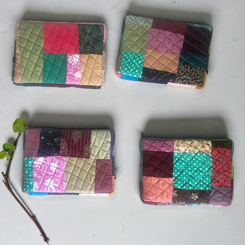 May include: Four colorful patchwork laptop sleeves. Each sleeve features a unique arrangement of quilted fabric squares in various colors, including pink, green, and burgundy. The sleeves have a zipper closure and a quilted texture.