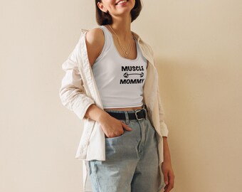 May include: A white crop top with the text "Muscle Mommy" and a barbell graphic. The model is wearing the top with a white button-down shirt and blue denim shorts.