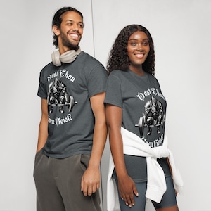 May include: Two people wearing dark gray t-shirts with a graphic of a knight lifting weights and the text "Dost Thou Even Hoist?". The shirts are short-sleeved and made of a soft material.