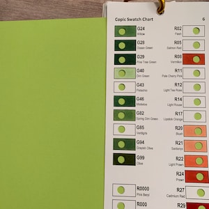 Op de afbeelding: Een Copic Swatch Chart met kleurstalen in groene en rode tinten. De kaart bevat kleurnamen en -nummers voor elke tint. De kaart is gelabeld met "Copic Swatch Chart" en "6".